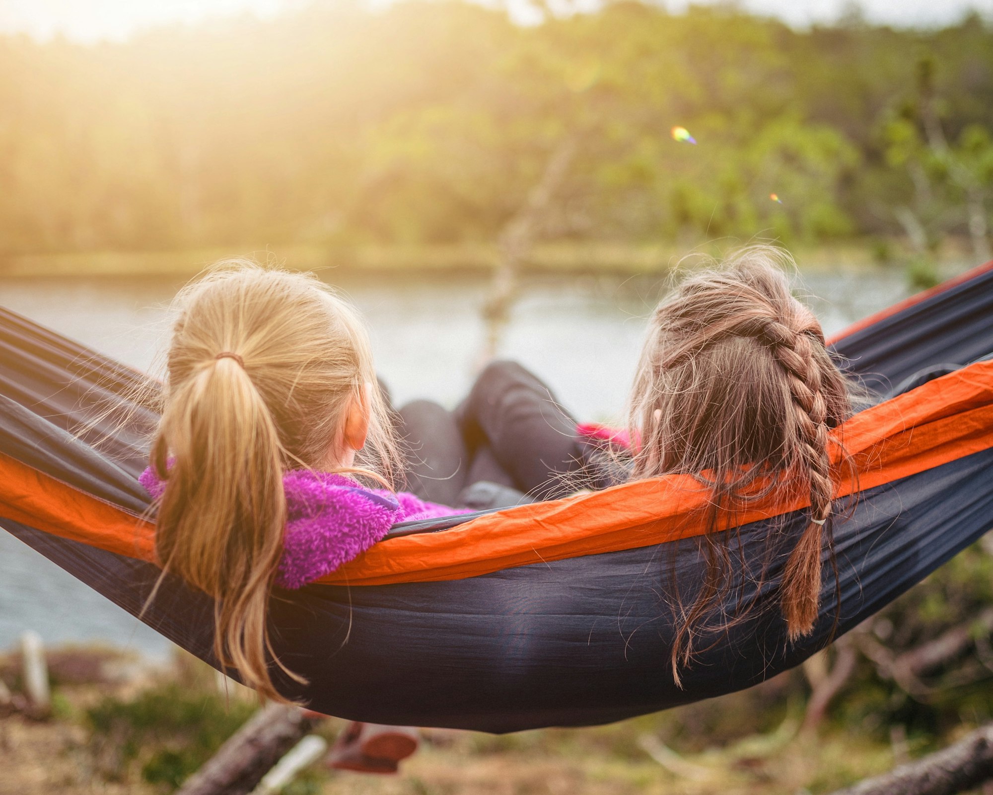 Two girls are side-by-side in a hammock, facing away from the camera.