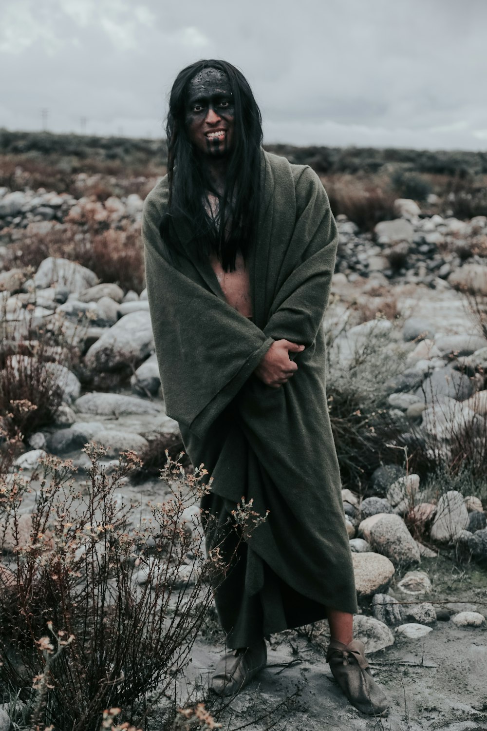 person covering blanket and standing near rocks during daytime