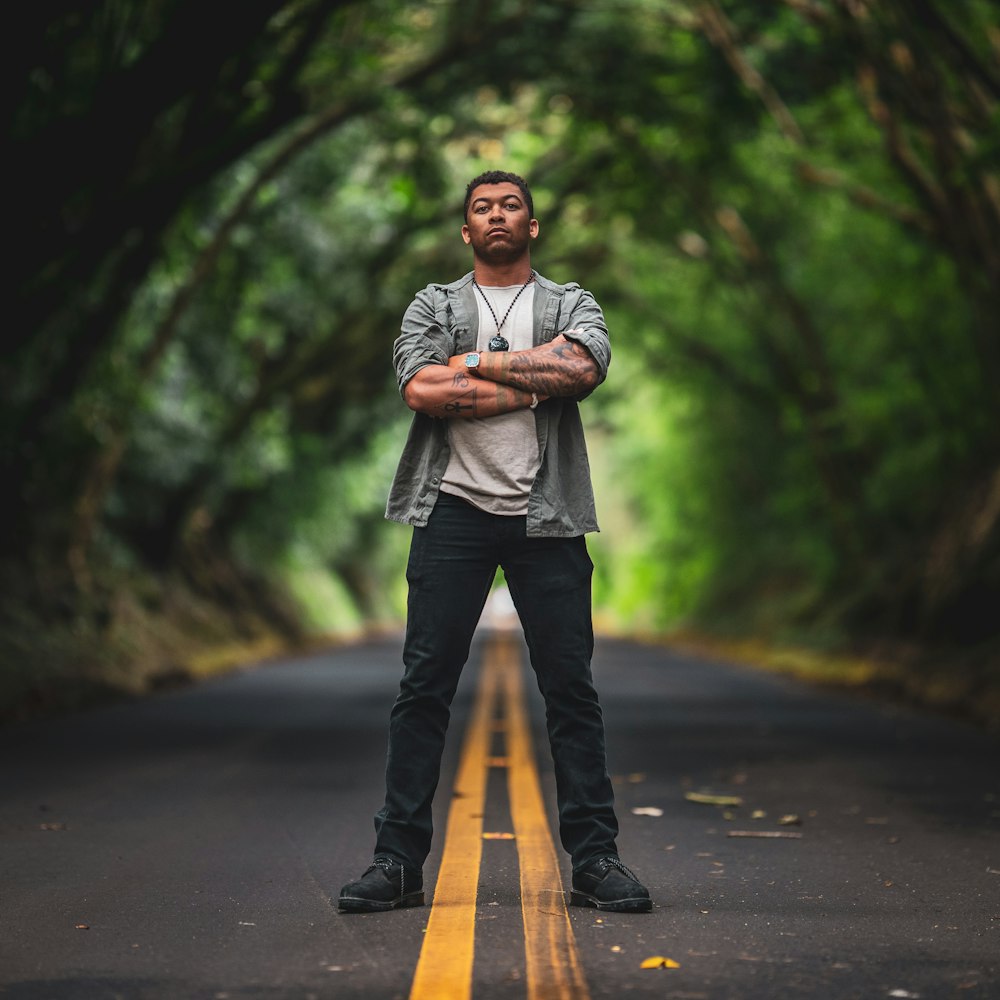 man standing in the middle of the road under trees