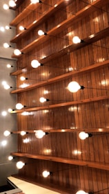 Wooden panels arranged horizontally with numerous bright light bulbs suspended from the ceiling, creating a pattern of light and shadows.
