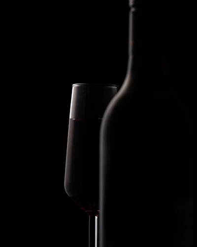 Cinematic shot of a bottle of fine wine and crystal glass with deep shadows and warm lighting