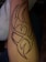 An arm with a large tribal tattoo in dark ink featuring a complex geometric pattern of sharp, interconnected lines and curves. The tattoo covers a significant portion of the forearm.