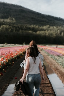 two girl walking near flower field during daytime