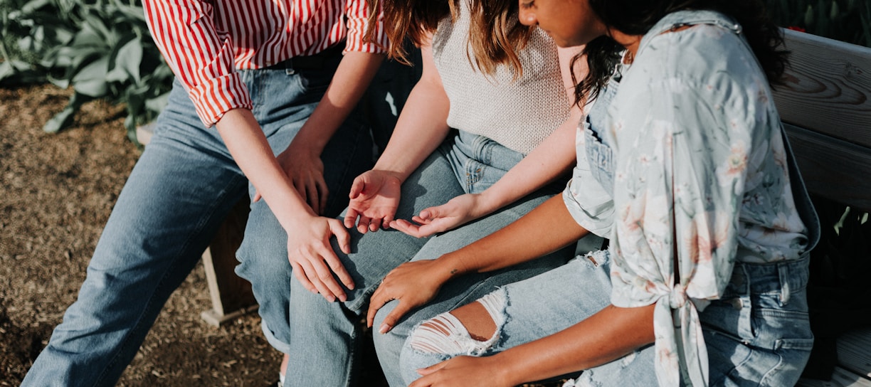 three women wearing blue denim jeans sitting on gray wooden bench