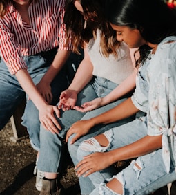 three women wearing blue denim jeans sitting on gray wooden bench