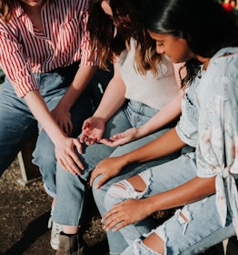 three women wearing blue denim jeans sitting on gray wooden bench