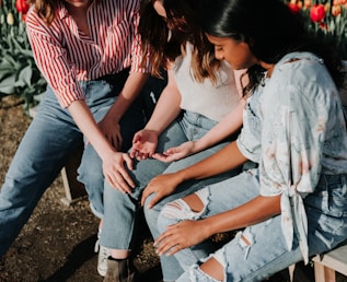 three women wearing blue denim jeans sitting on gray wooden bench