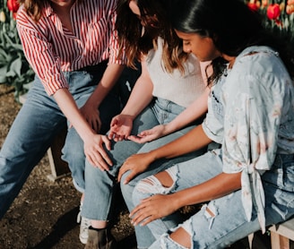 three women wearing blue denim jeans sitting on gray wooden bench