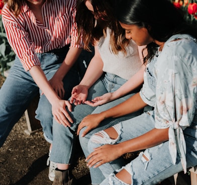 three women wearing blue denim jeans sitting on gray wooden bench