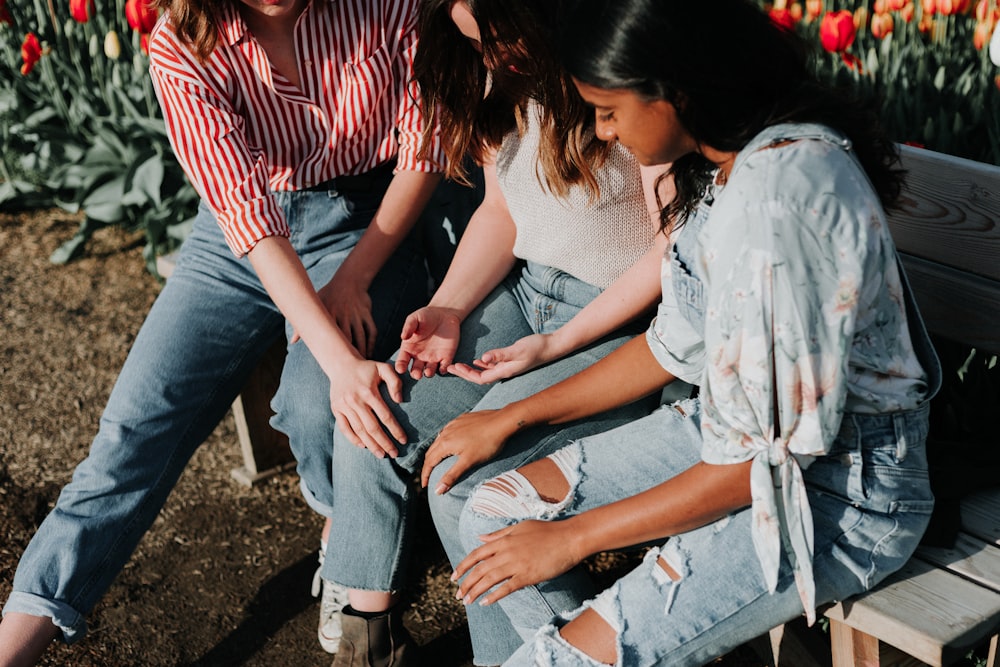 three women wearing blue denim jeans sitting on gray wooden bench