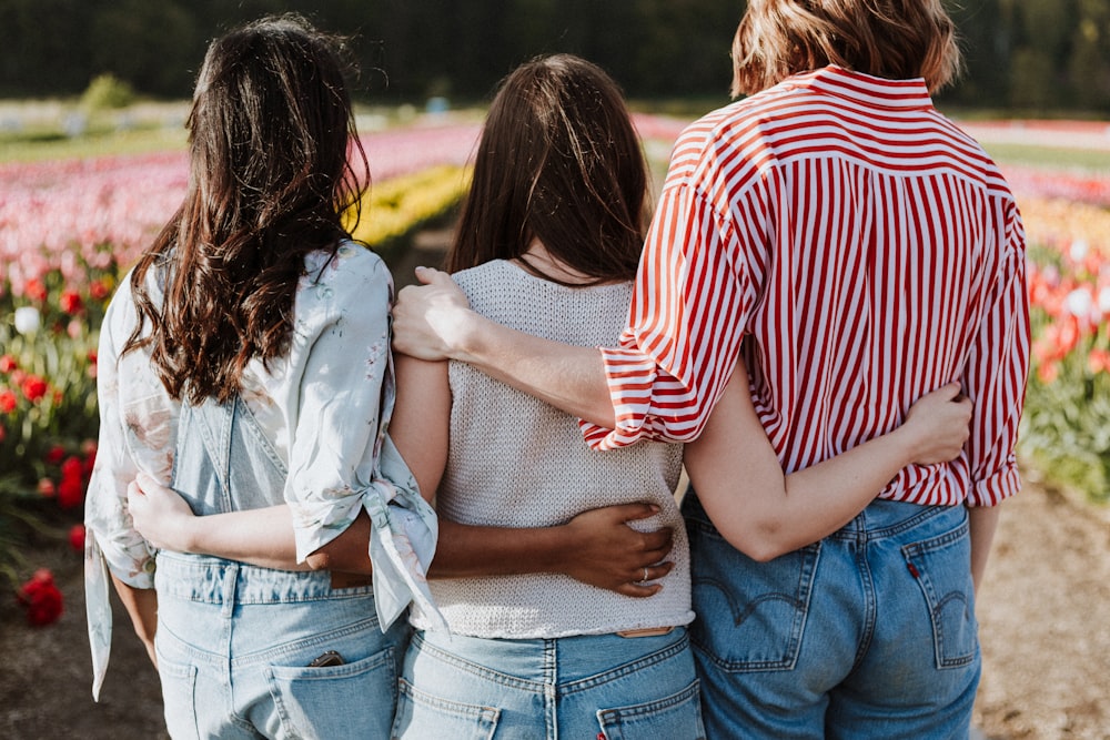 trois femmes se tenant la main devant un jardin de fleurs