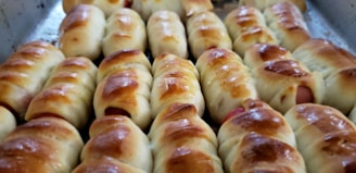 A tray filled with freshly baked bread rolls wrapped around sausages, with a golden-brown crust.