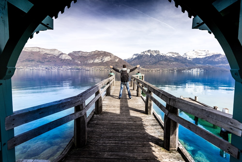 person raising both hands standing on pathway near body of water