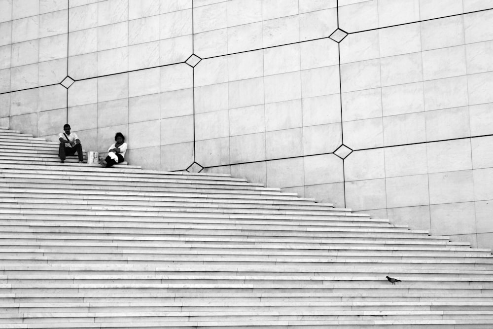 Foto in scala di grigi di coppia di uomo e donna seduta sulle scale