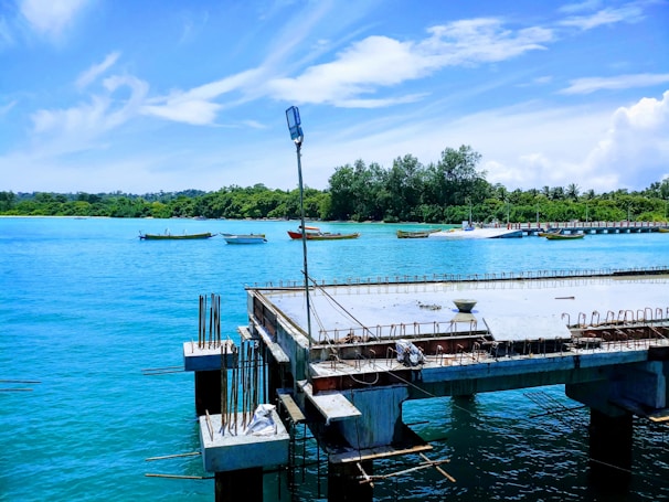 Engineers inspecting a waterfront pier structure with calm water and boats in the background.