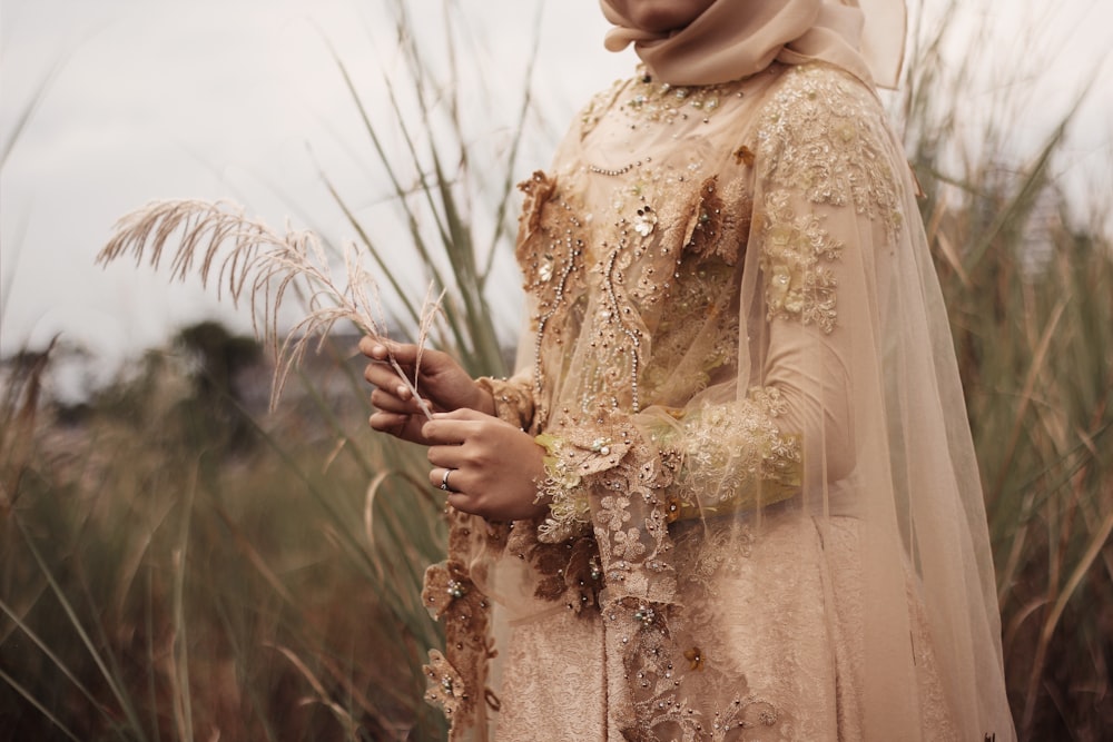 woman in beige floral embroidered wedding dress stands in grass field