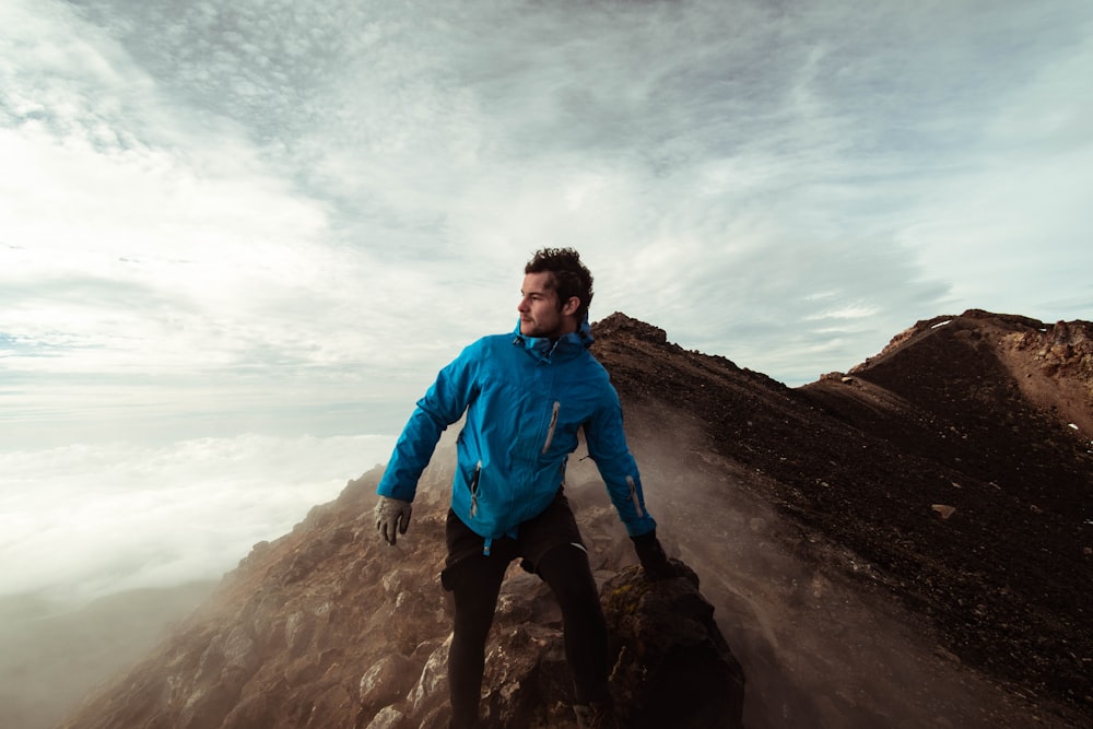man in blue jacket standing on cliff