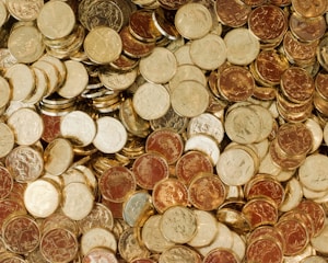 A large pile of mixed coins, predominantly of Australian origin, with varying shades of gold and copper. The coins are densely packed and form a textured, reflective surface.