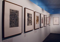 Wide shot of a modern black gallery wall displaying several original paintings with spot lighting.