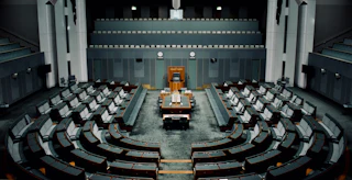 An empty modern legislative chamber with curved empty desks facing a raised wooden podium