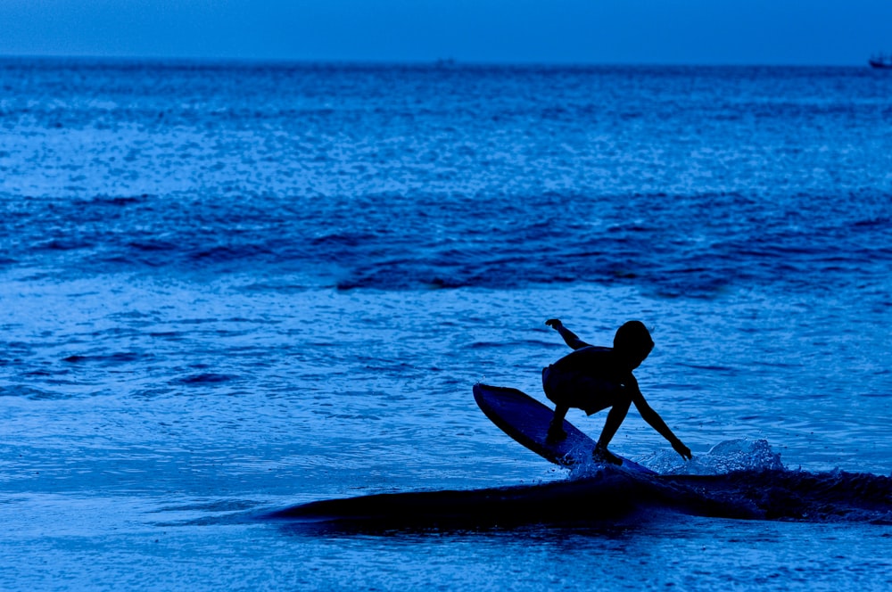 silhouette of boy on surfboard out at blue sea