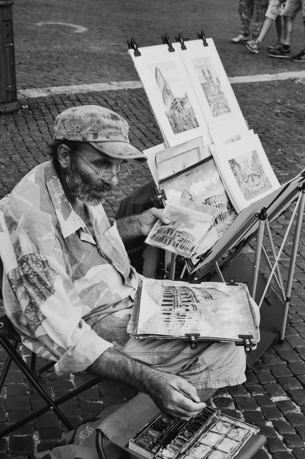 man sitting beside folding table with paintings