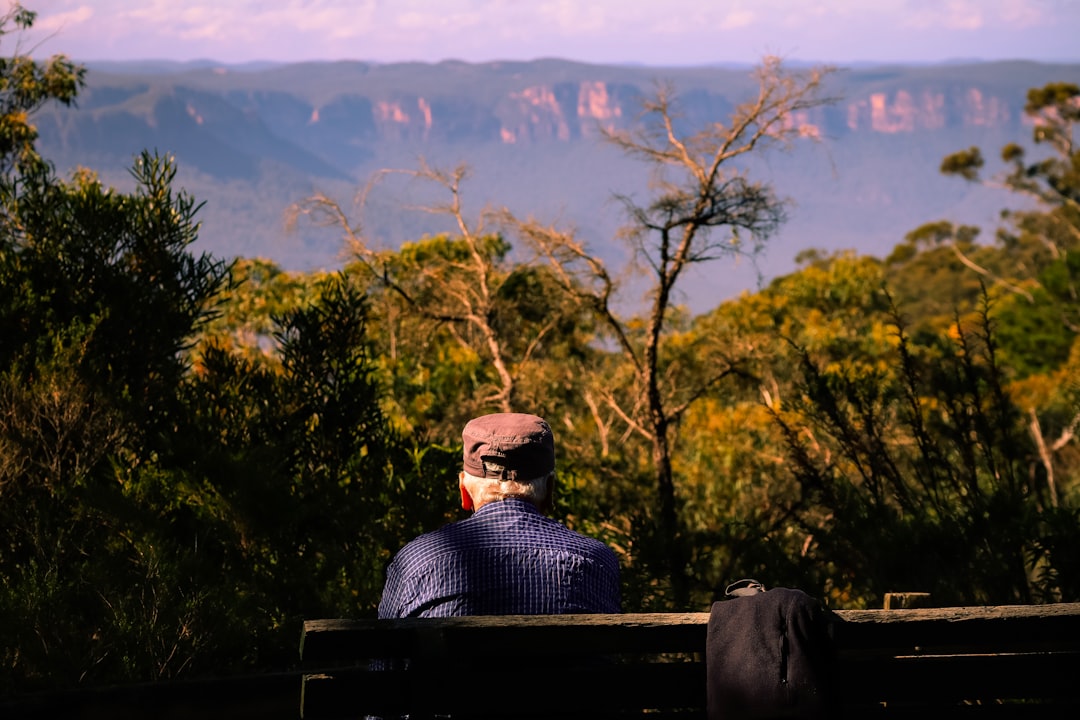man in blue shirt on park bench facing mountain in horizon