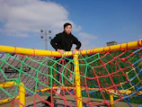 A climbing net structure with children playing energetically on a sunny day.