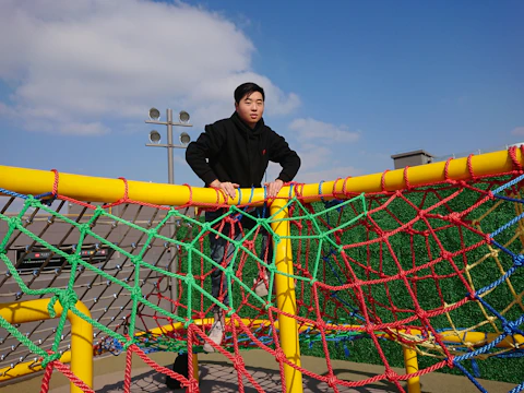 A climbing net structure with children playing energetically on a sunny day.