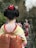 A person dressed in traditional Japanese attire is seen from behind, wearing a kimono with intricate floral patterns and an obi with red and gold designs. The hairstyle is elaborate, adorned with colorful hair ornaments.