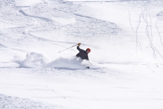A skier in vibrant gear carving through fresh powder on a sunny mountain slope.