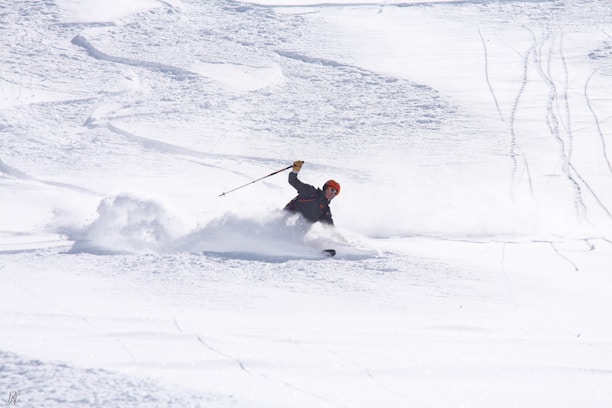 A skier in vibrant gear carving through fresh powder on a sunny mountain slope.