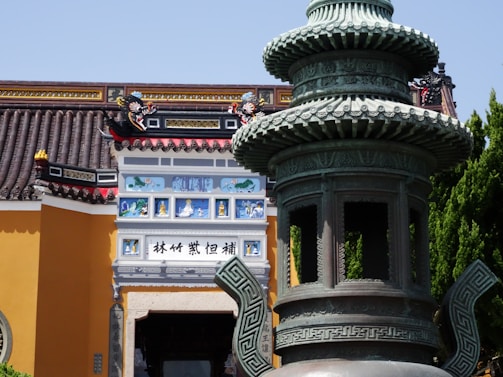 A detailed view of a traditional Asian architectural structure, featuring ornate designs with intricate details. A large decorative incense burner is in the foreground, with vibrant colors and elaborate carvings. The building displays vibrant paintings and sculptures, enhancing its cultural significance.