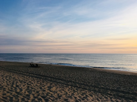 A tranquil beach scene at sunset with lounge chairs and gentle waves.