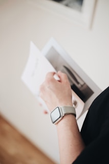 A hand holding an open magazine or booklet, showcasing a page with an image. The person is wearing a smartwatch on their wrist.