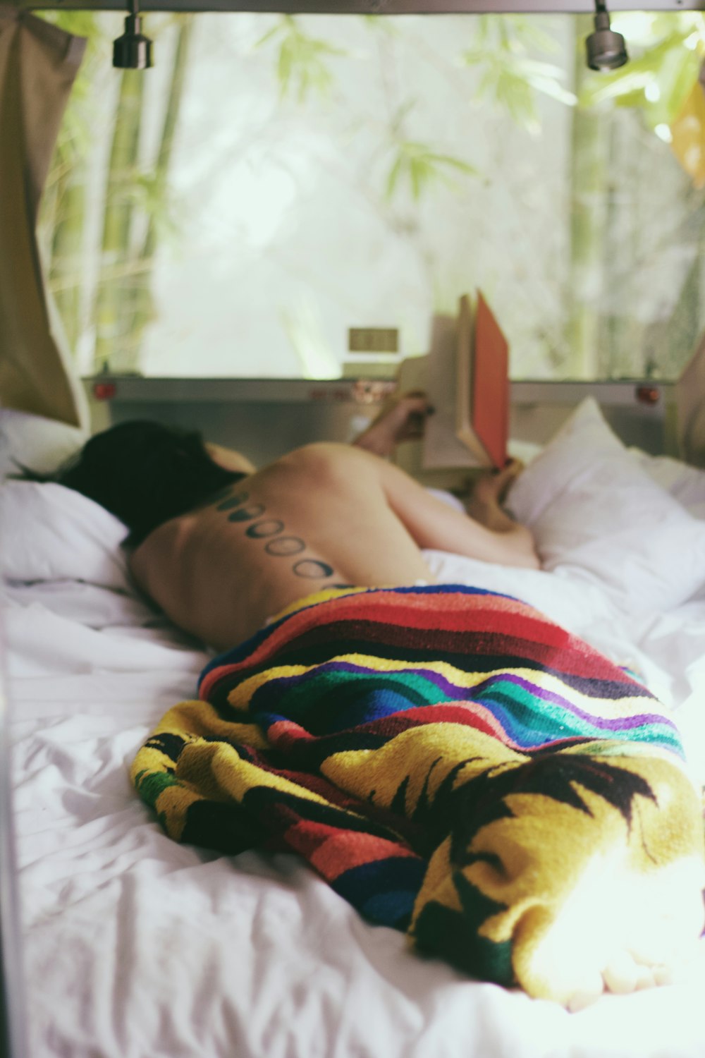 ベッドに横たわっているトップレスの人が本を読んでいる