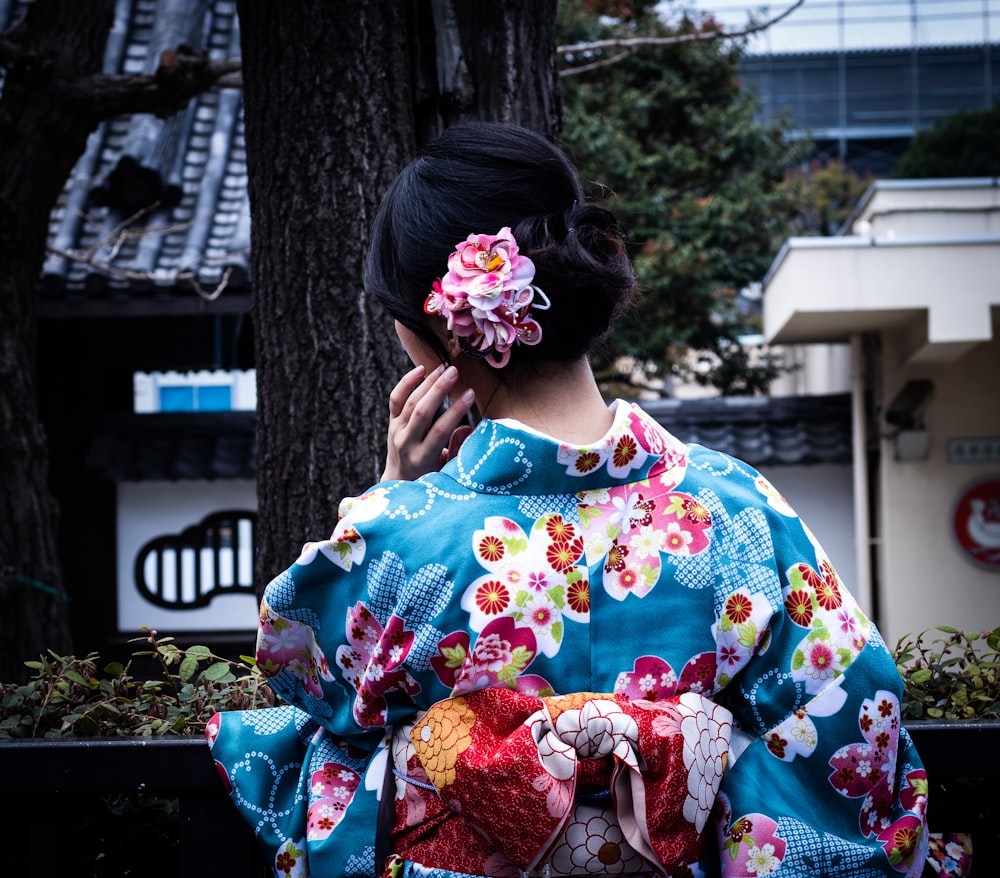 woman wearing blue and multicolored floral kimuno standing and facing near tree
