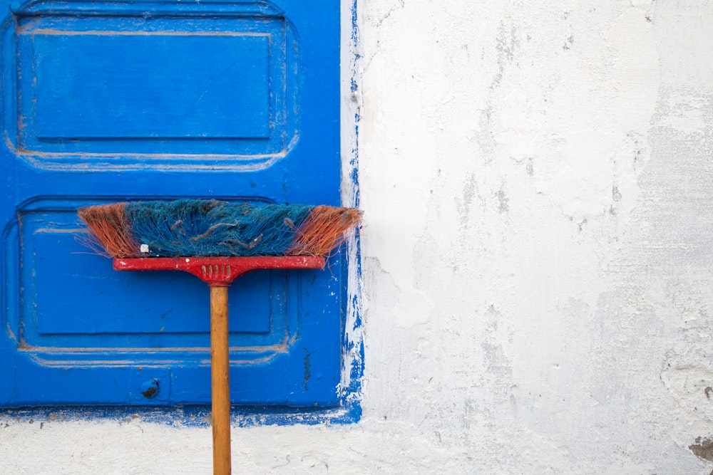 red and orange push boroom leaned on blue door