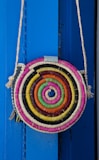Close-up of a colorful printed tote bag hanging on a hook against a bright wall.