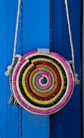 A colorful woven handbag hanging from a rustic hook against a textured wall.