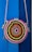 A round, woven bag with a colorful spiral pattern hangs against a vibrant blue background. The bag features concentric circles in shades of pink, orange, yellow, green, and blue, with a rope strap attached.