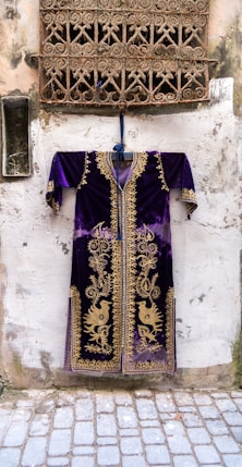 purple and gold long-sleeved dashiki dress hanging by a window