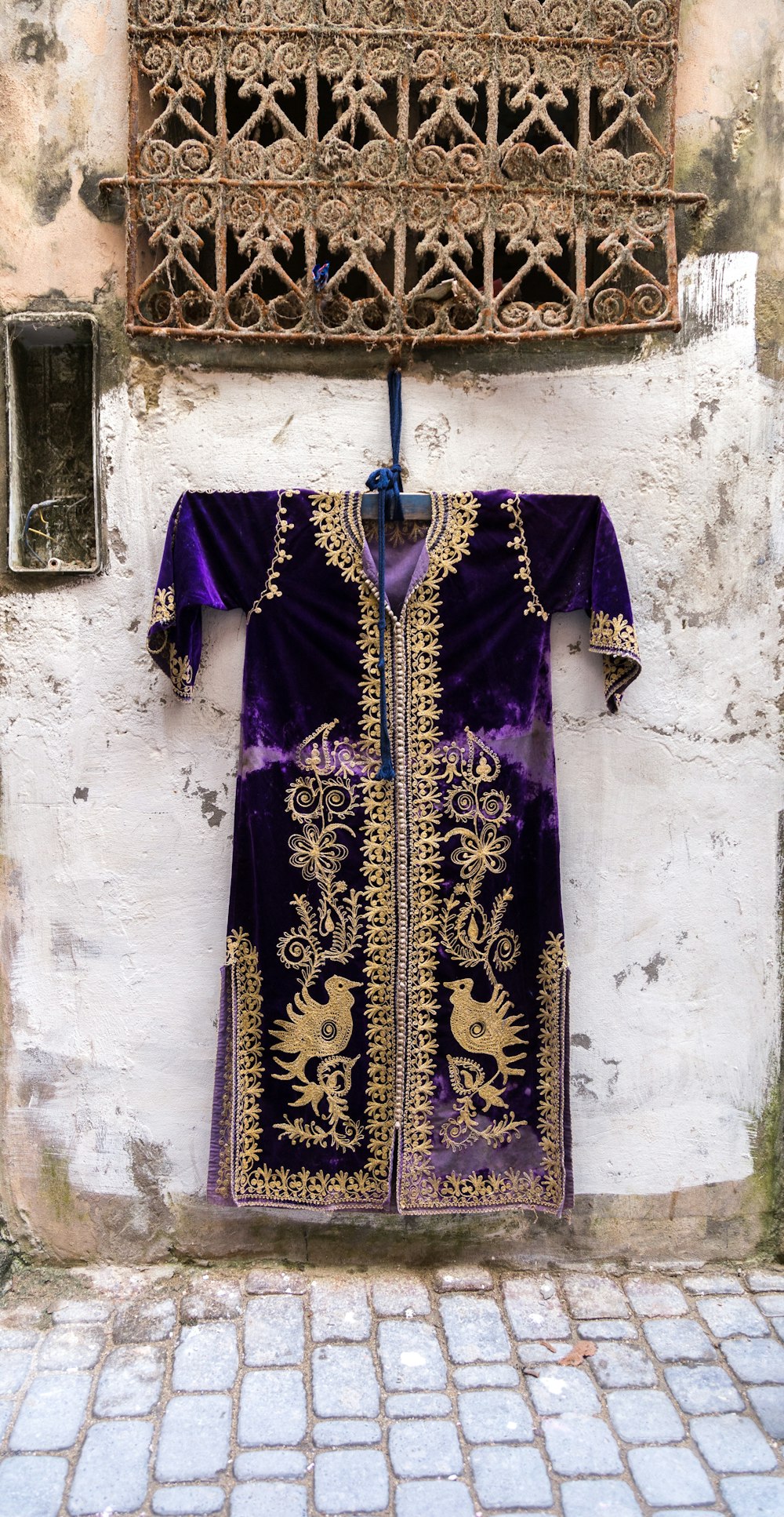 purple and gold long-sleeved dashiki dress hanging by a window