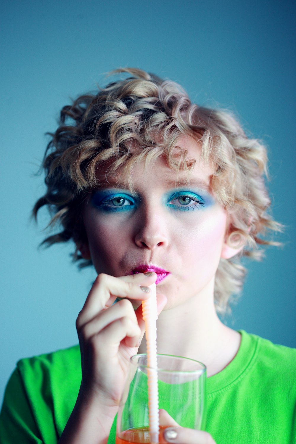 woman with blue eyemake up sipping beverage