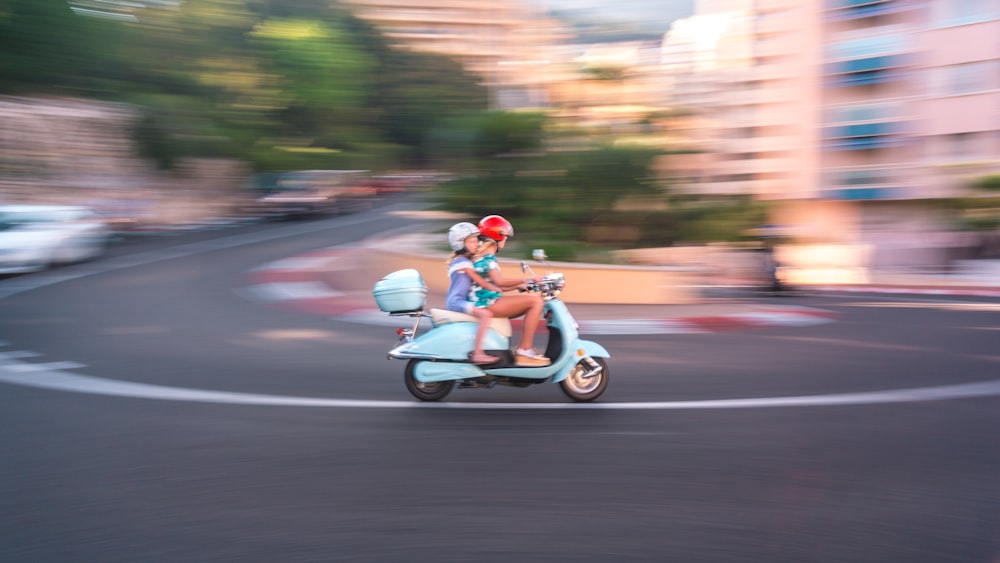 Zwei Personen fahren mit blauem Motorroller in der Stadt