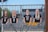 Four cutout images of people are mounted on a metal fence with a sports stadium in the background.