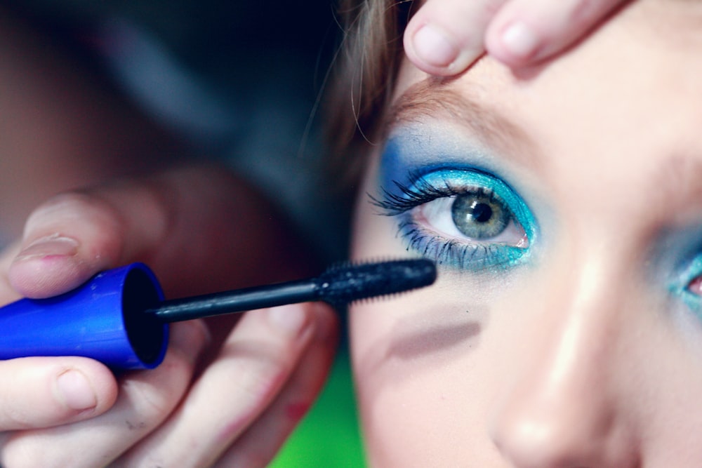 mascara being applied on woman's eyelash with blue eyeshadow