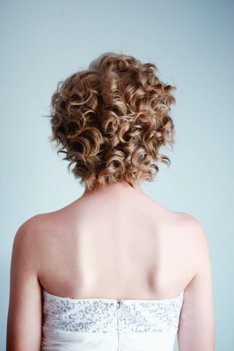 Short, bouncy golden curls cut into a rounded shape, seen from behind