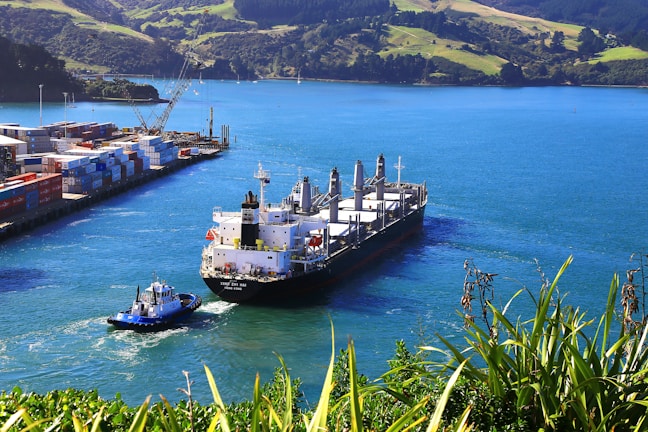 Aerial view of a large cargo ship being guided into port by tugboats, highlighting expert navigation.