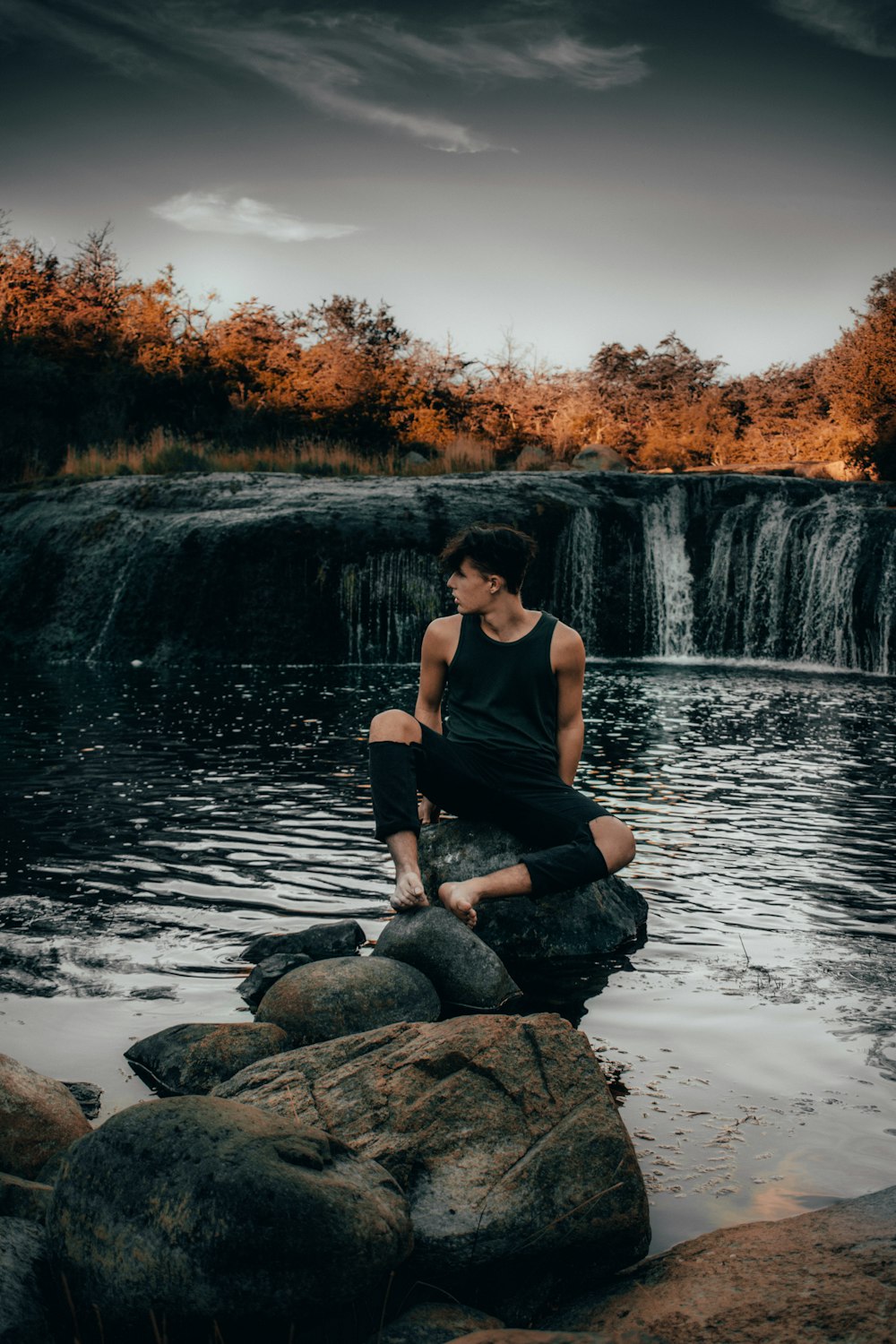 man sits on rock near falls